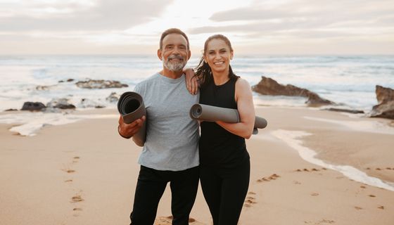 Zwei glückliche und sportliche ältere Menschen am Strand mit einer Gymnastikmatte. 