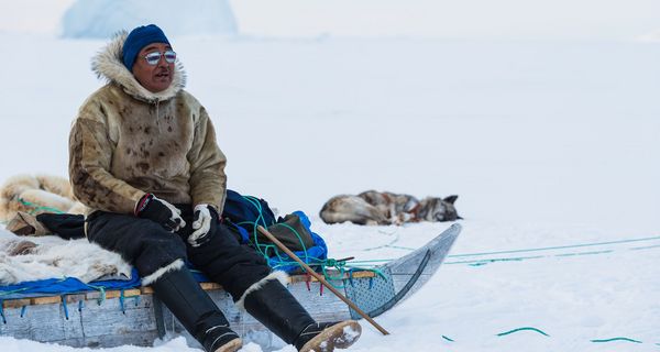 Inuit in einer Schneelandschaft auf einem Hundeschlitten.