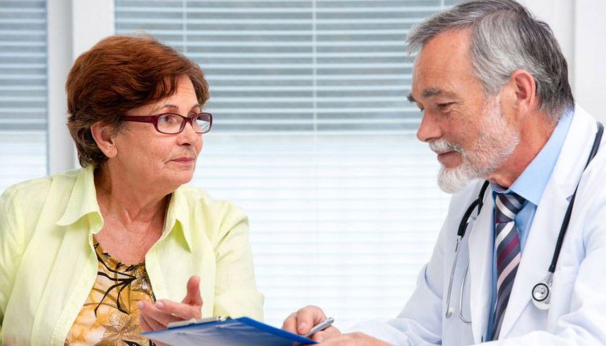 Arzt sitzt gemeinsam mit einer Patient an einem Tisch und erklärt ein Dokument.