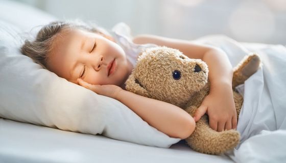 Mädchen schläft mit Teddy im Arm.