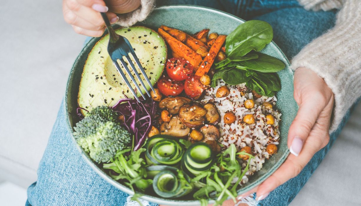 Frau hat eine Vegetarische Bowl auf dem Schoß mit diversen gesunden, pflanzlichen Bestandteilen