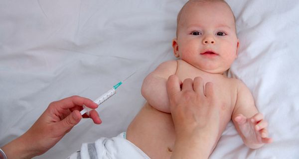Baby auf dem Rücken liegend mit Einmalwindel bekleidet und Hand mit einer Impfspritze