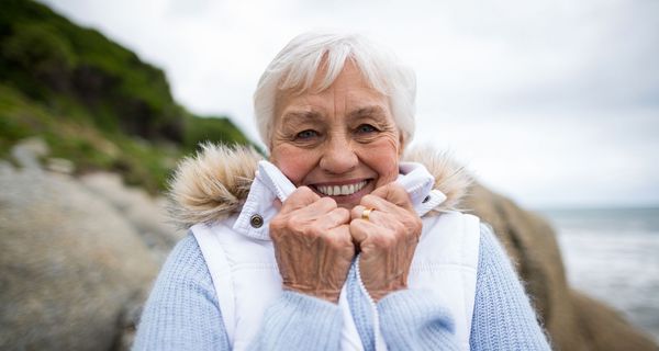 Ältere Dame mit warmer Kleidung am Strand, winterlich.