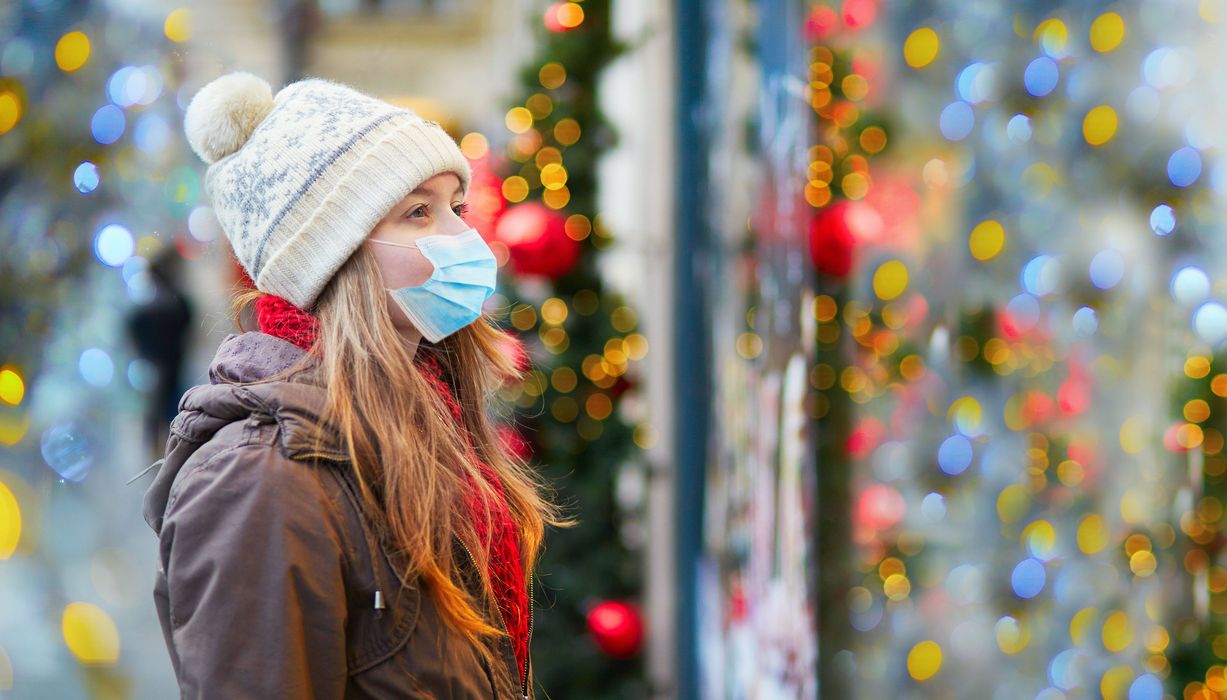 Frau mit Mütze und Maske, steht vor einem weihnachtlich geschmückten Schaufenster.