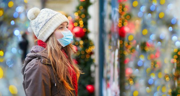 Frau mit Mütze und Maske, steht vor einem weihnachtlich geschmückten Schaufenster.