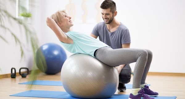 Ältere Frau, macht Rücken-Übungen auf einem großen Gymnastik-Ball.