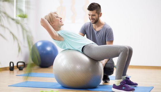 Ältere Frau, macht Rücken-Übungen auf einem großen Gymnastik-Ball.