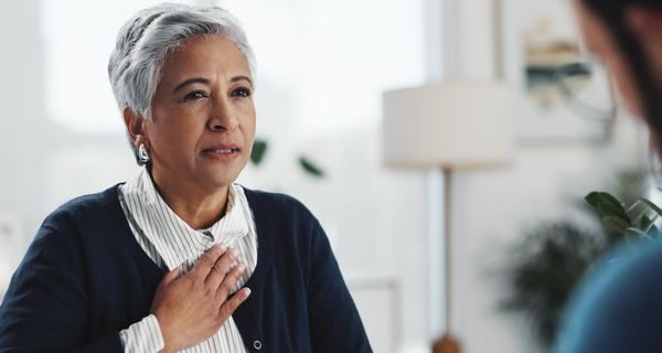 Eine ältere Frau hält sich die Hand auf die Brust.