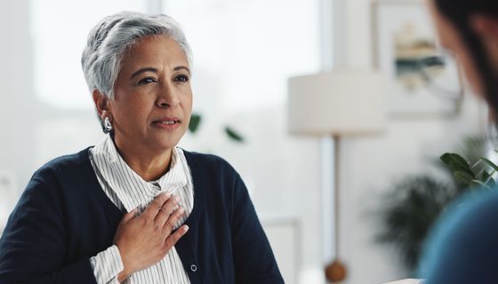 Eine ältere Frau hält sich die Hand auf die Brust.