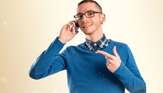 Dünner Mann in den 30ern in blauem V-Pullover beim Telefonieren