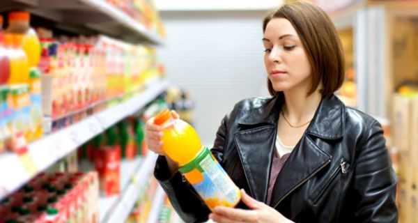 Junge Frau im Supermarkt, betrachtet das Etikett von einer Flasche Orangensaft.