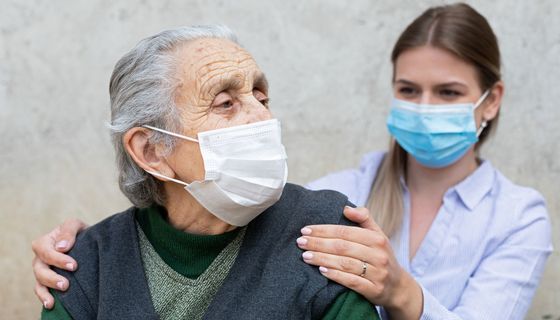 Alte Frau mit Maske, dahinter eine junge Frau, ebenfalls mit Maske.