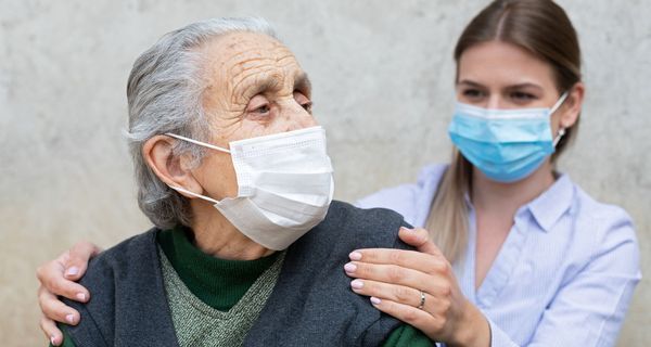 Alte Frau mit Maske, dahinter eine junge Frau, ebenfalls mit Maske.