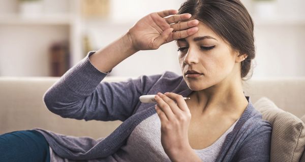 Frau, liegt auf der Couch und misst Fieber.