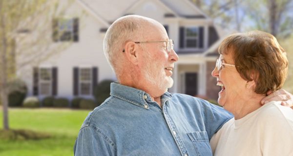 Rentnerpaar im Freien vor ihrem Haus; schauen sich lachend an