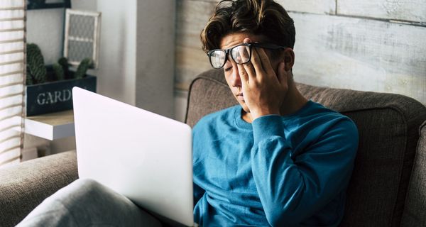 Junger Mann, müde mit Laptop auf der Couch.