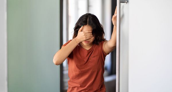 Frau, hält sich an einer Wand fest.