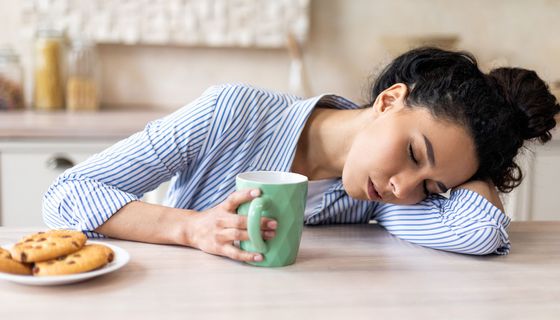 Junge Frau, morgens müde mit einer Tasse Kaffee und einem Teller Keksen.