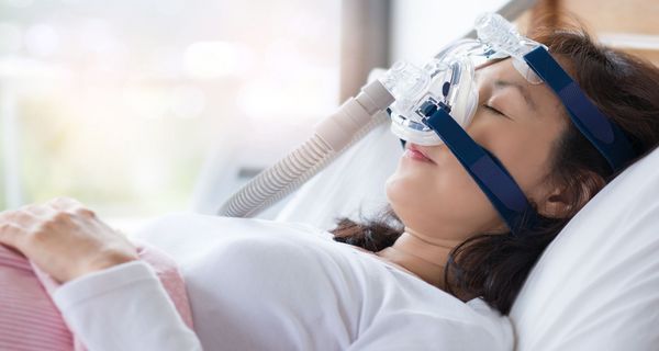 Frau liegt mit Überdruckmaske im Bett.