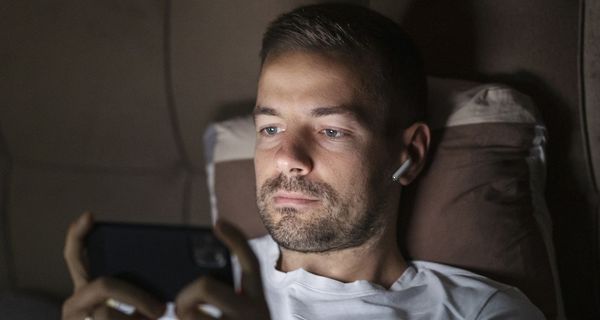 Mann über 40 liegt im Bett. Sein Smartphone erhellt sein Gesicht.