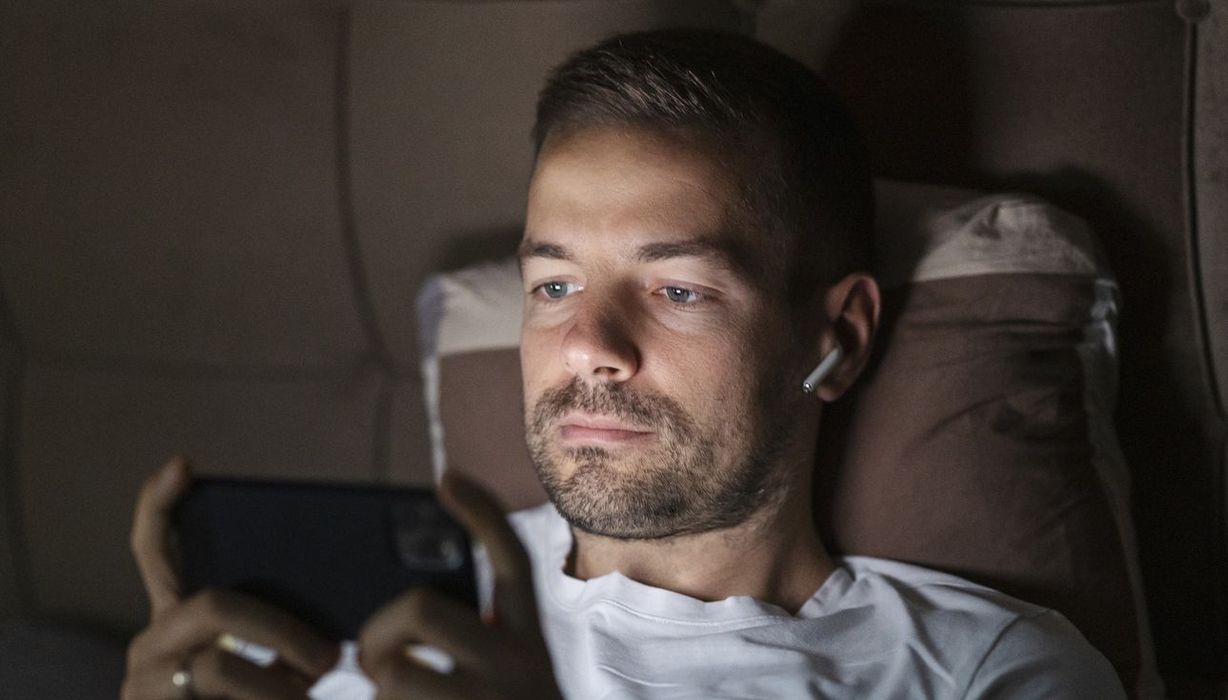 Mann über 40 liegt im Bett. Sein Smartphone erhellt sein Gesicht.
