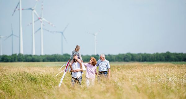 Eltern mit Kind und Großeltern gehen auf einer Wiese vor mehreren Windrädern spazieren.