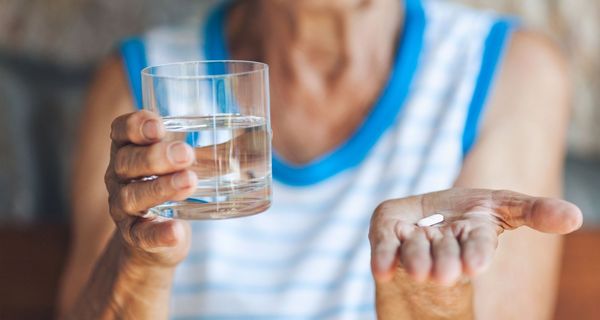 Ältere Frau, hält ein Glas Wasser und eine Tablette in den Händen.