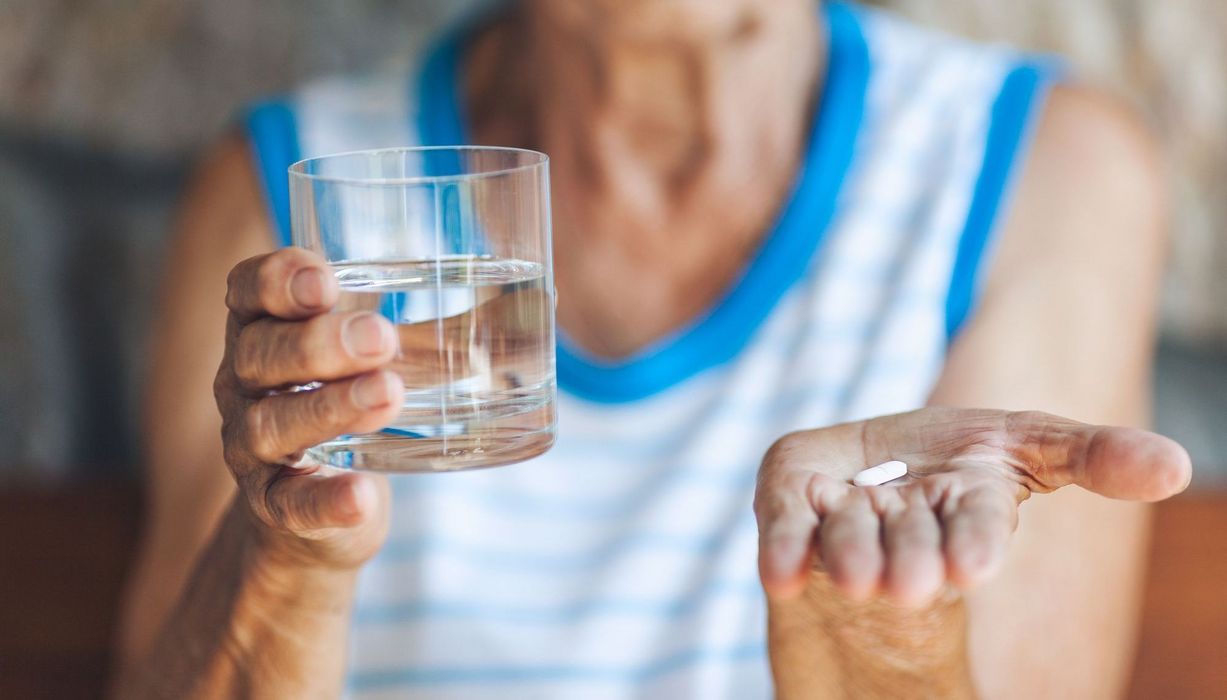 Ältere Frau, hält ein Glas Wasser und eine Tablette in den Händen.