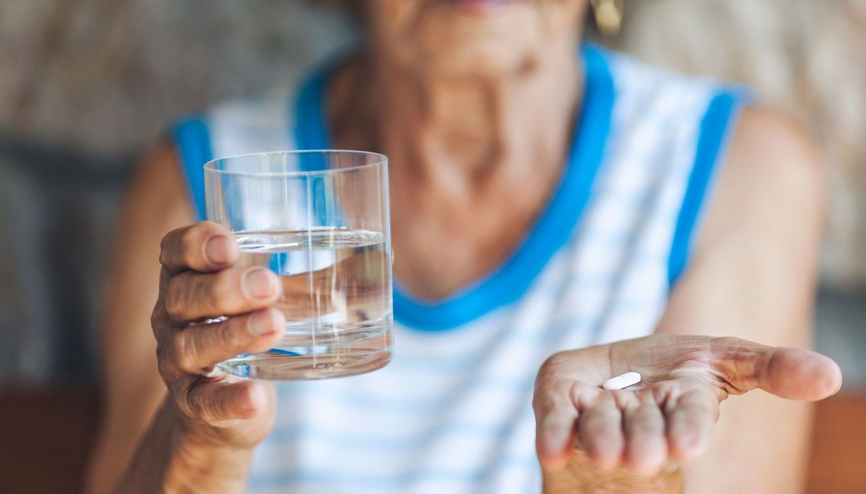 Ältere Frau mit Wasserglas und Tablette.