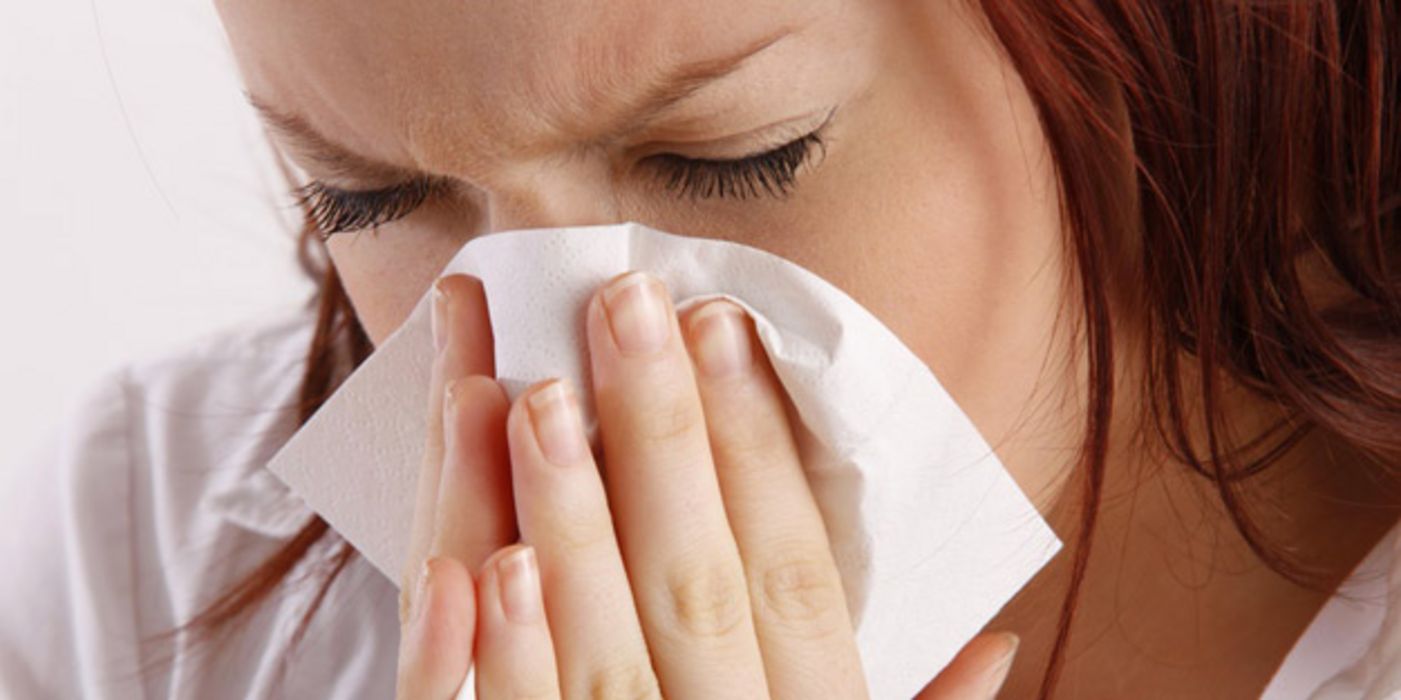 Erkältete Frau putzt sich die Nase.