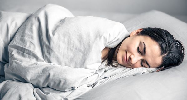 Frau, liegt unter einer Decke und schläft.