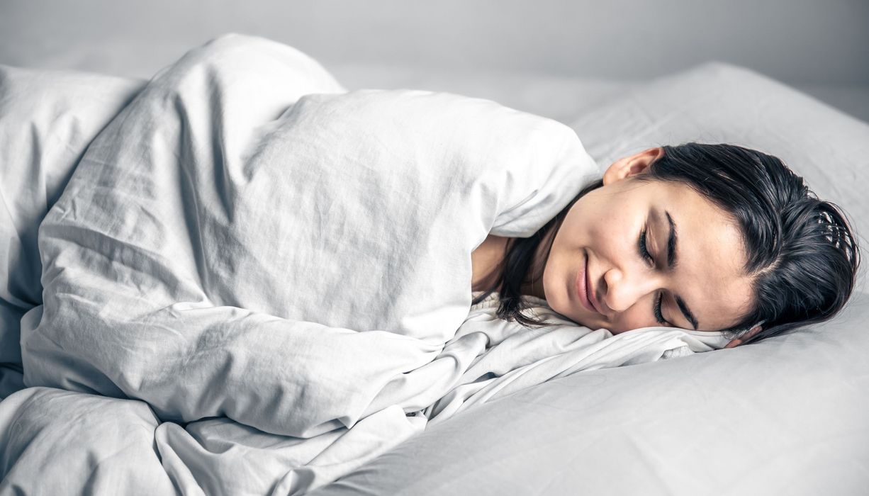 Frau, liegt unter einer Decke und schläft.