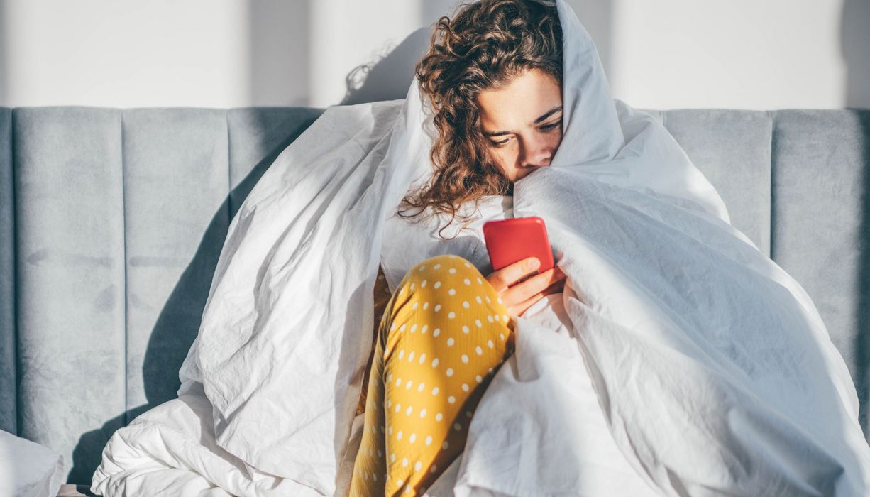 Frau mit Decke und Smartphone.