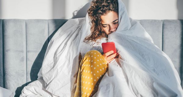 Frau mit Decke und Smartphone.