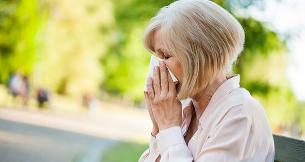 Frau, sitzt draußen auf einer Bank und putzt sich die Nase.