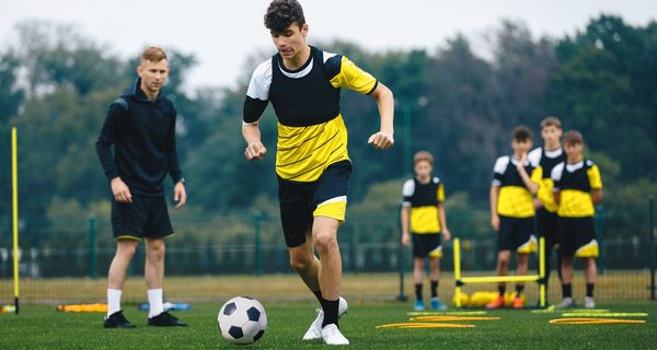 Junge Fußballer machen auf einem Trainingsplatz Aufwärmübungen. Ein Trainer steht daneben.  
