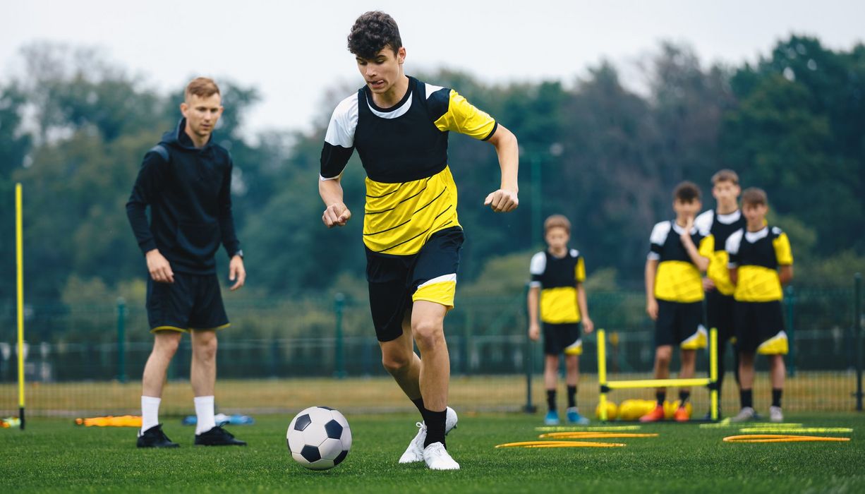 Junge Fußballer machen auf einem Trainingsplatz Aufwärmübungen. Ein Trainer steht daneben.  