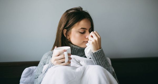 Frau sitzt mit einer Tasse Tee im Bett, hat Schnupfen. 