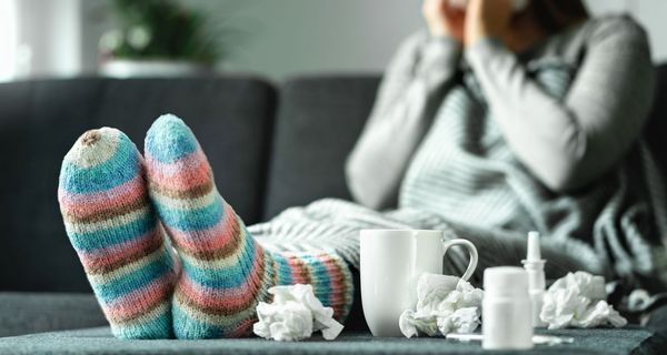 Frau mit bunten, dicken Socken, einer Teetasse und Taschentüchern.