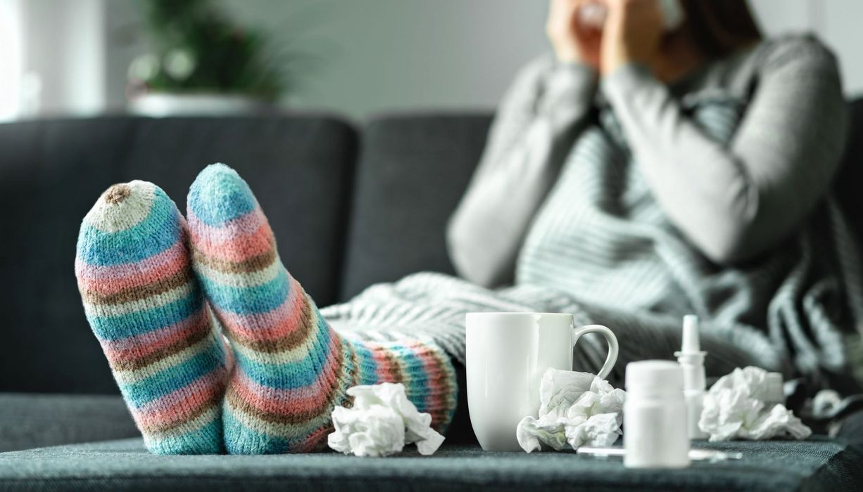 Frau mit bunten, dicken Socken, einer Teetasse und Taschentüchern.