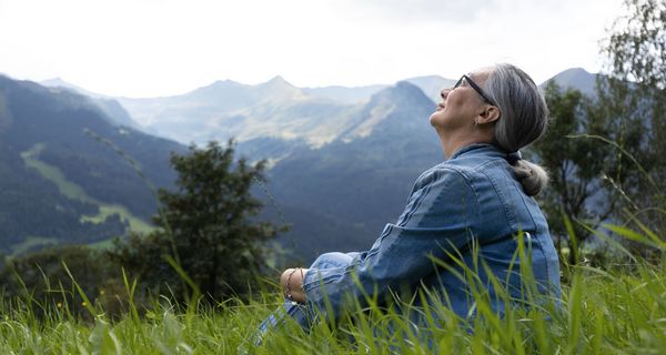 Ältere Frau, sitzt im Gras und schaut in den Himmel.