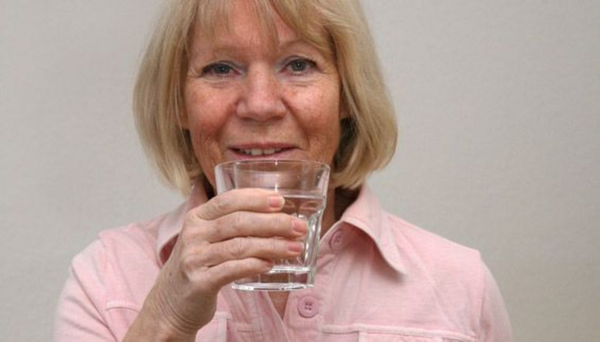 Frau in den Wechseljahren trinkt stehend ein Glas Wasser