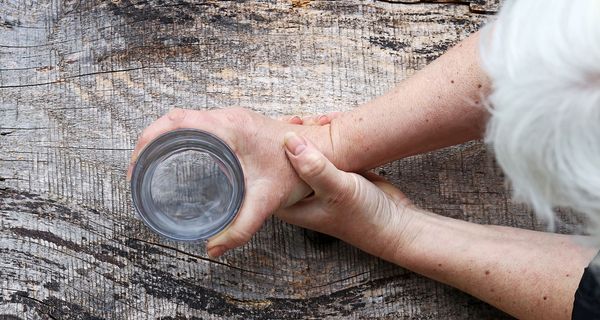 Ältere Frau, hält ein Wasserglas mit zitternder Hand.