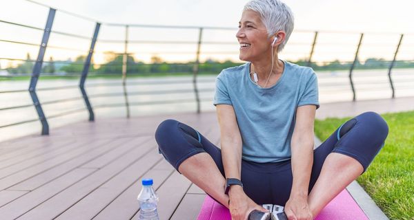 Seniorin in Sportkleidung, sitzt draußen und dehnt sich.