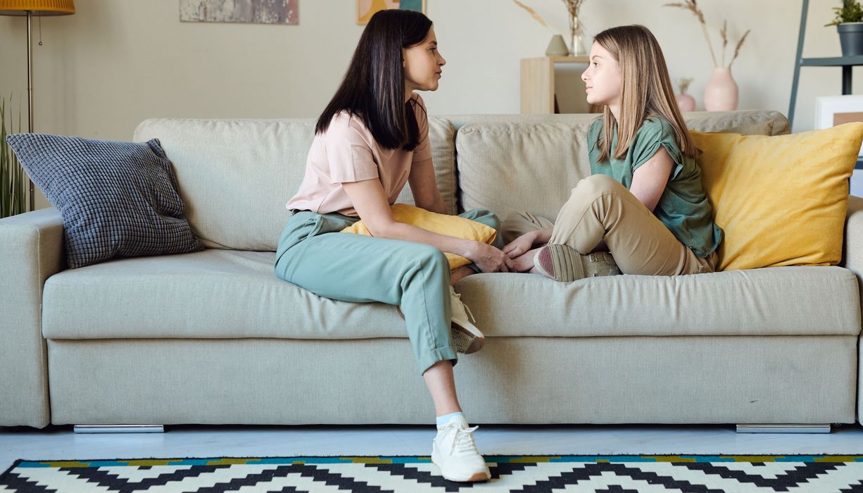 Zwei Mädchen sitzen auf einem Sofa und unterhalten sich.