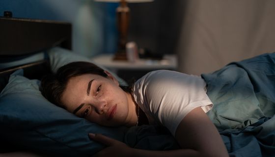 Frau, liegt im Bett und ist erschöpft.