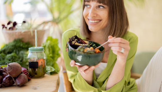 Junge Frau in grüner Bluse isst lächelnd Salat.