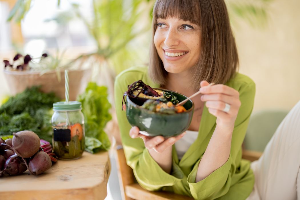 Junge Frau in grüner Bluse isst lächelnd Salat.