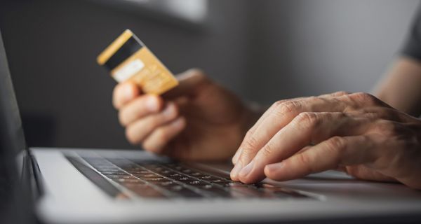 Online Bezahlung: Männerhände halten eine Kreditkarte und bedienen das Maus-Pad eines Laptops.
