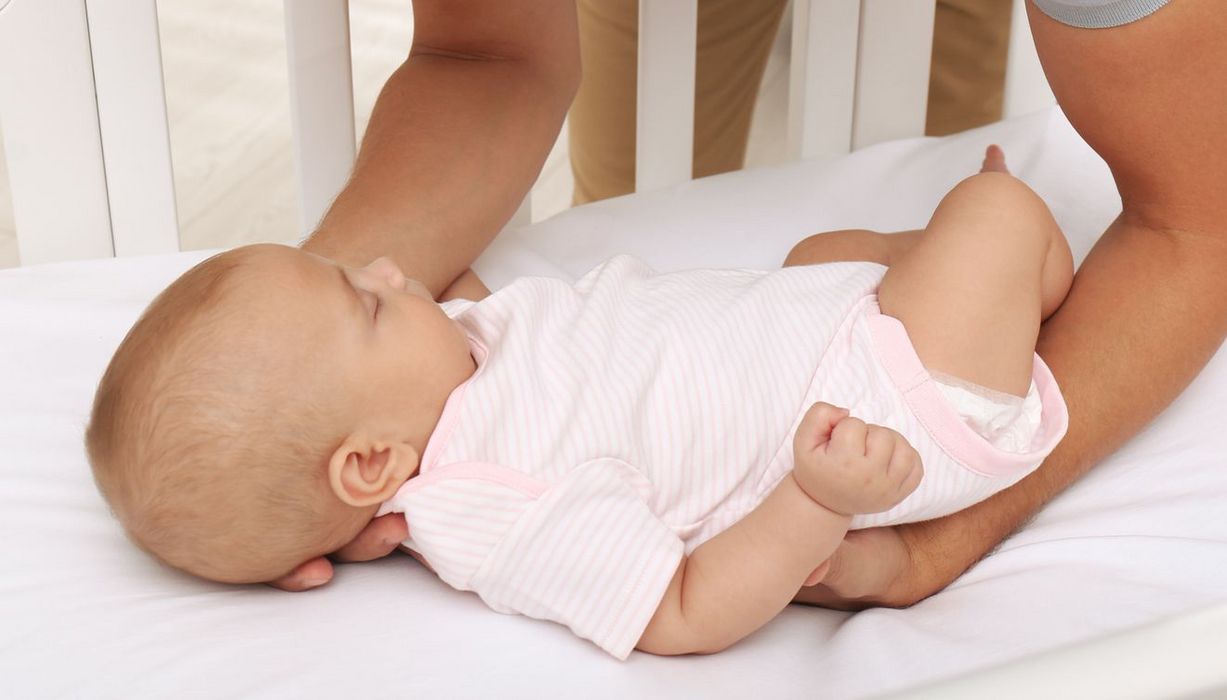 Schlafendes Baby wird auf den Rücken in seinem Bettchen gelegt.